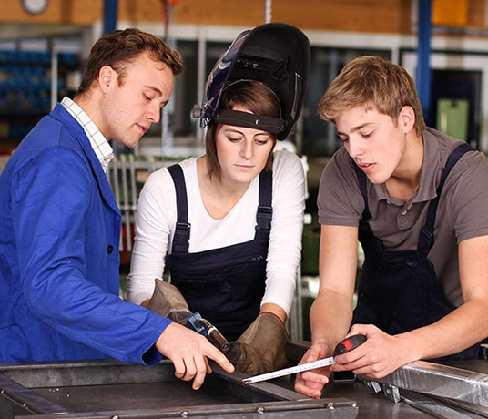 Apprentis en soudure travaillent ensemble en atelier.